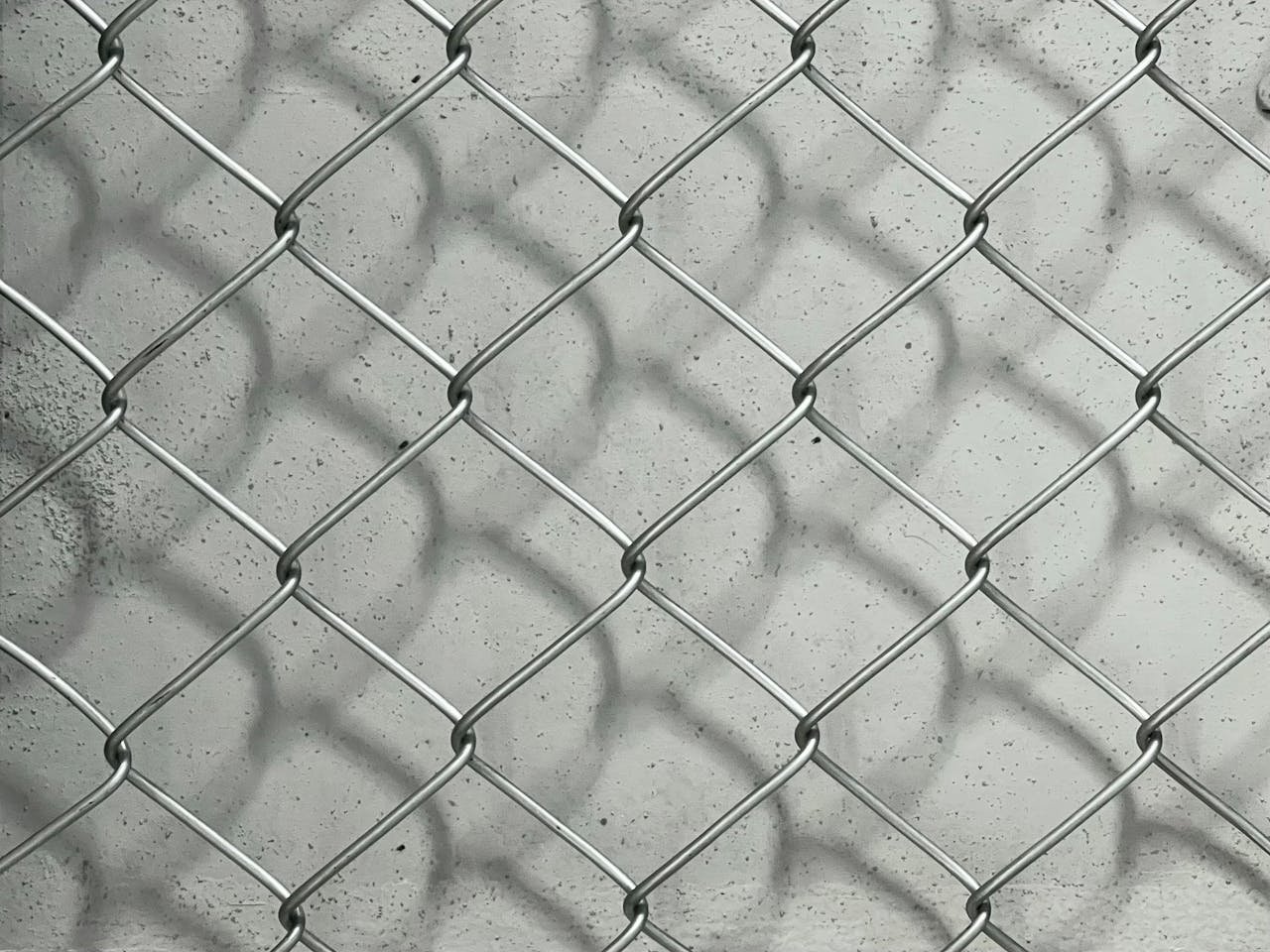 Detailed view of a metal chain link fence casting shadows on a concrete surface.